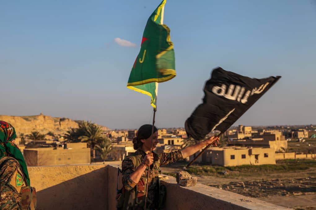 A YPJ fighter removes a Daesh flag and replaces it with a YPJ one